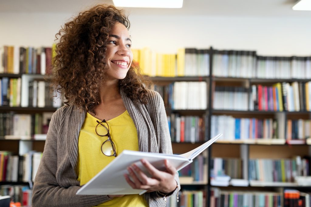 woman in library holding book and smiling