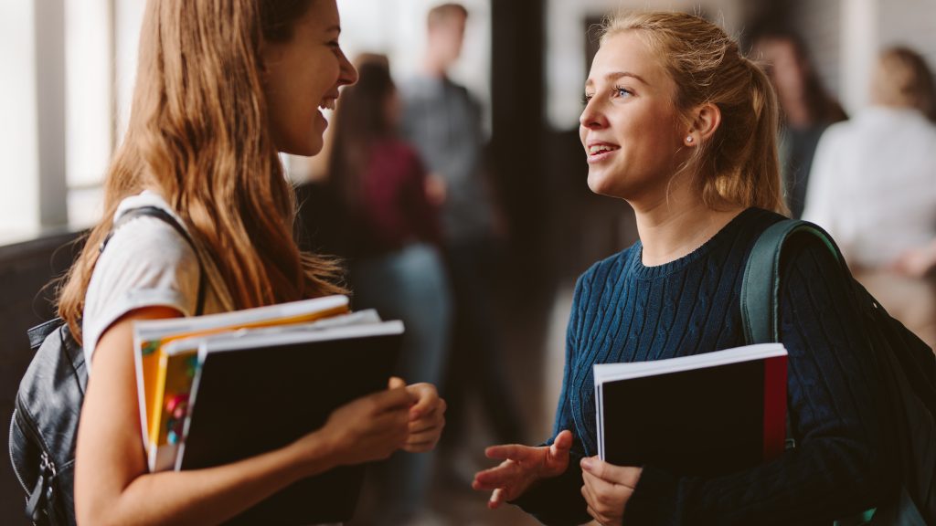 two women holding books and talking